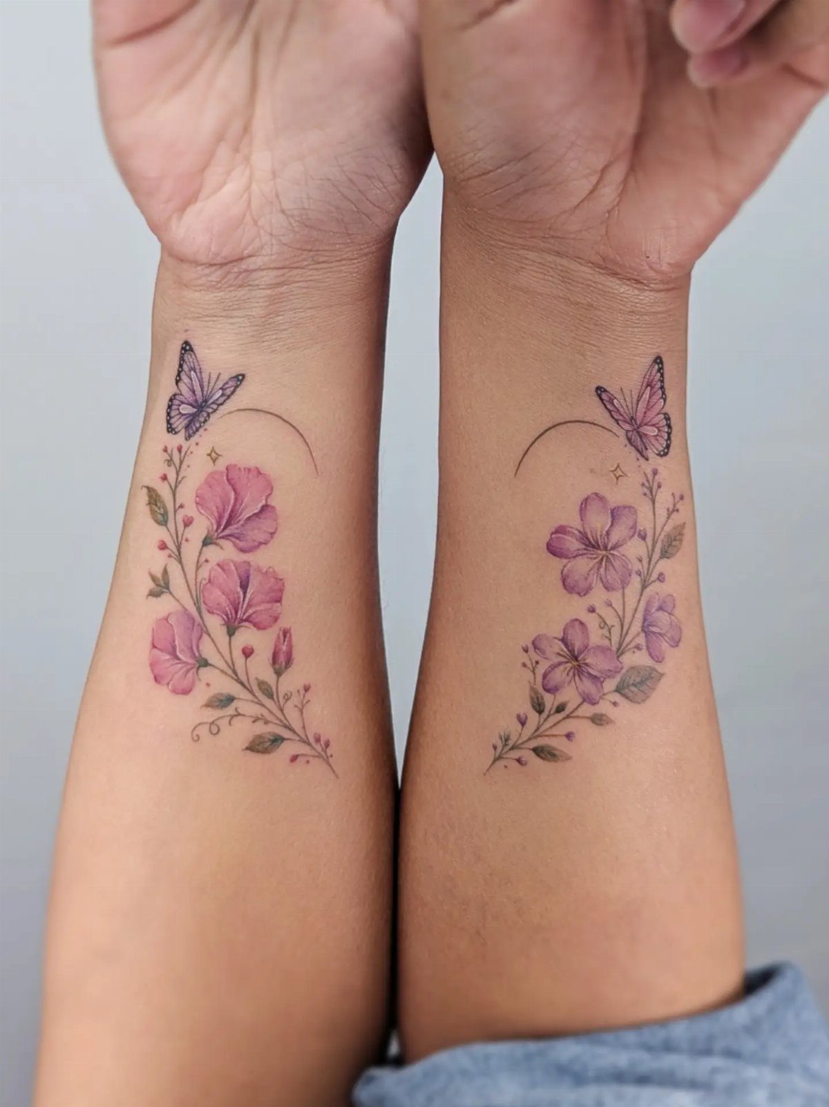 Pink flower and purple butterfly tattoos on two inner wrists and forearms.