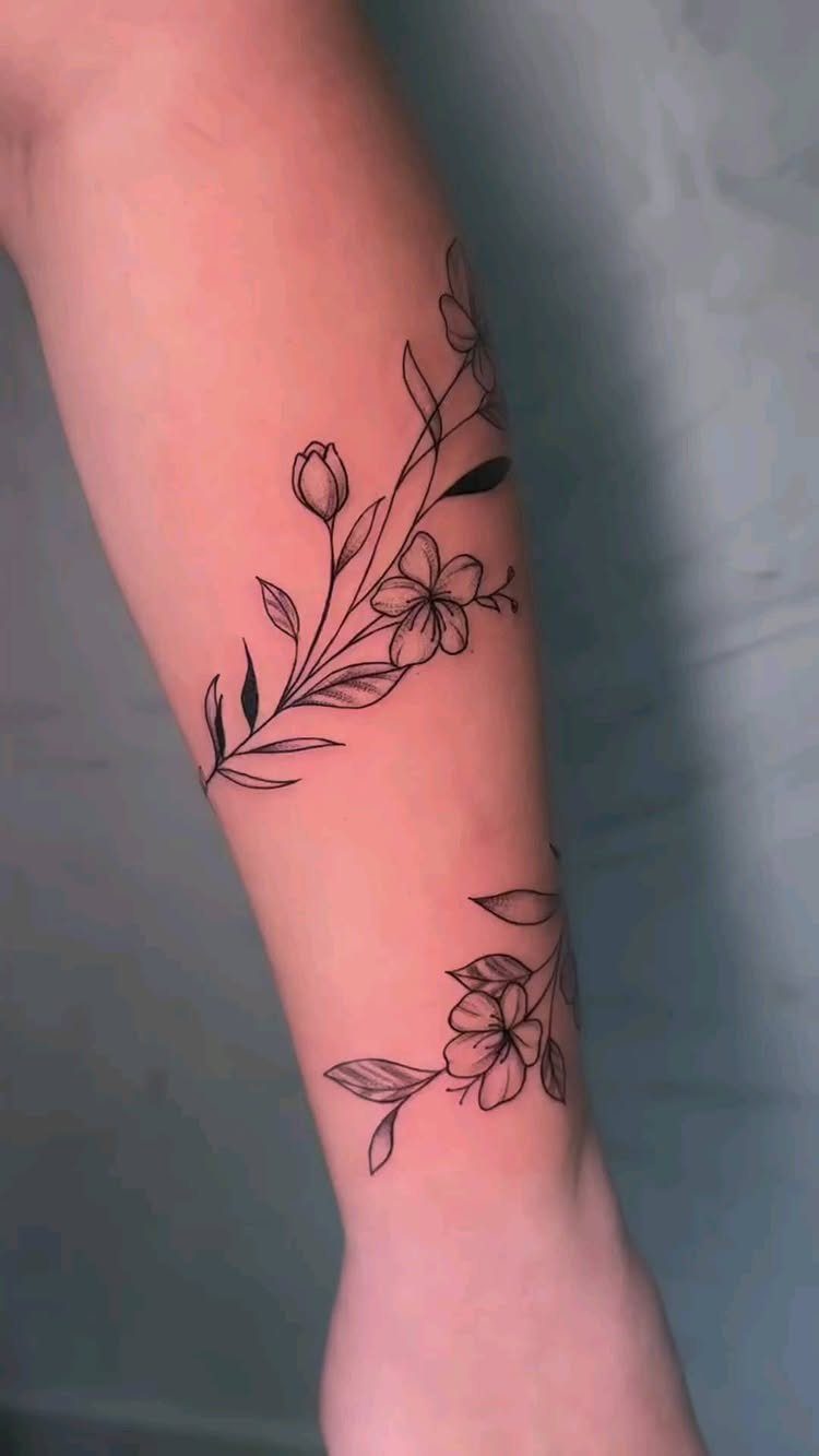Fine-line floral tattoos on a forearm and wrist featuring delicate black ink blossoms.