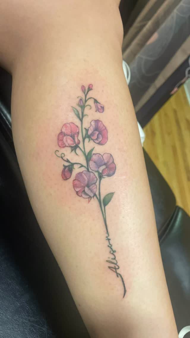 Sweet pea flower tattoo with the name Alison on a person's forearm