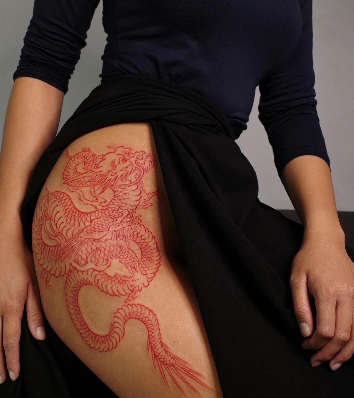 Red dragon tattoo on a person's thigh, featuring intricate scales and winding body.