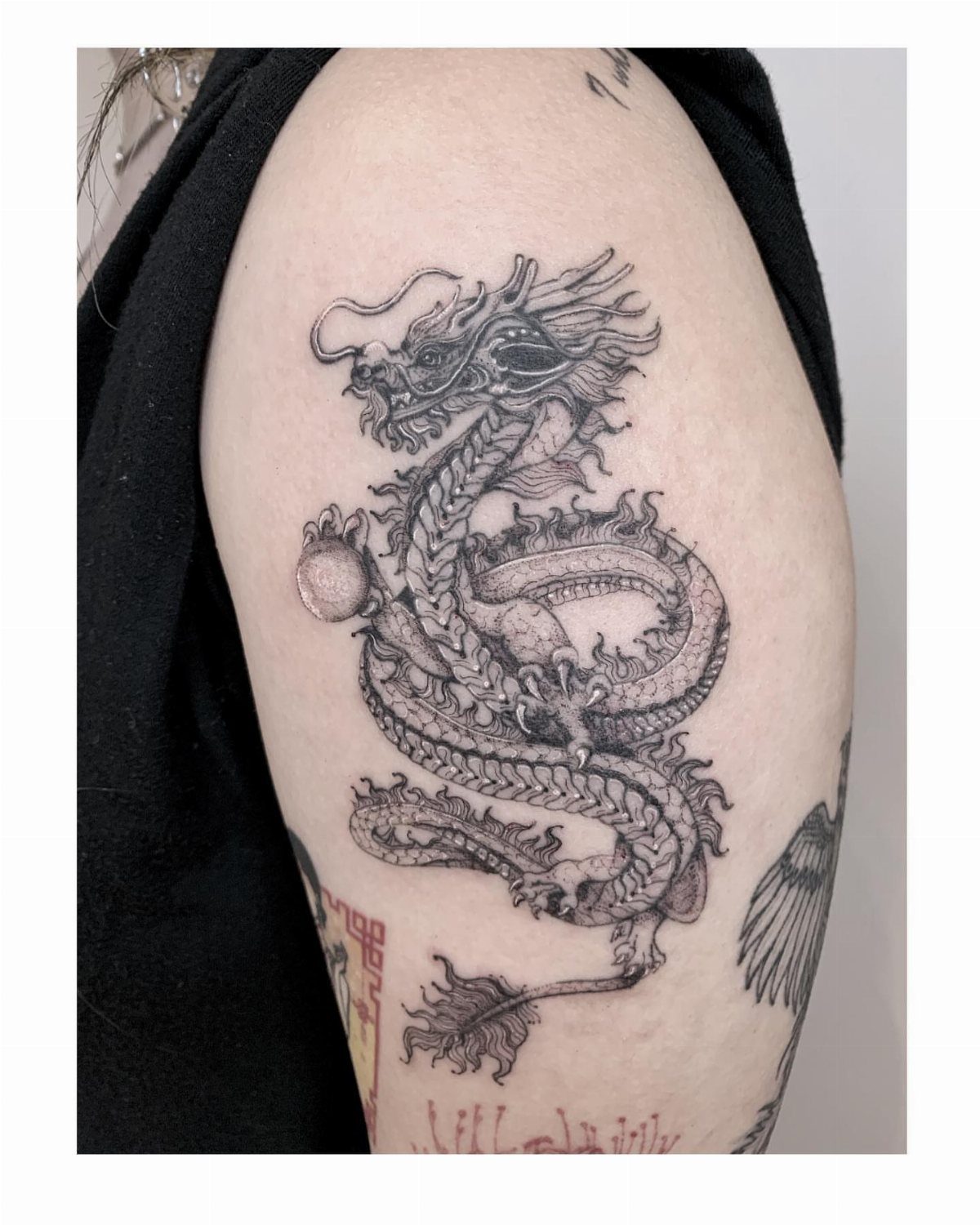 Asian dragon tattoo on an arm clutching a small circular pearl