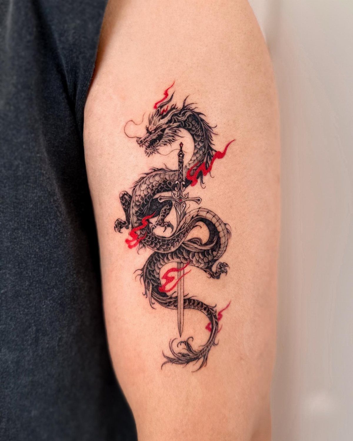 Asian dragon tattoo wrapped around a sword with red flames on an arm