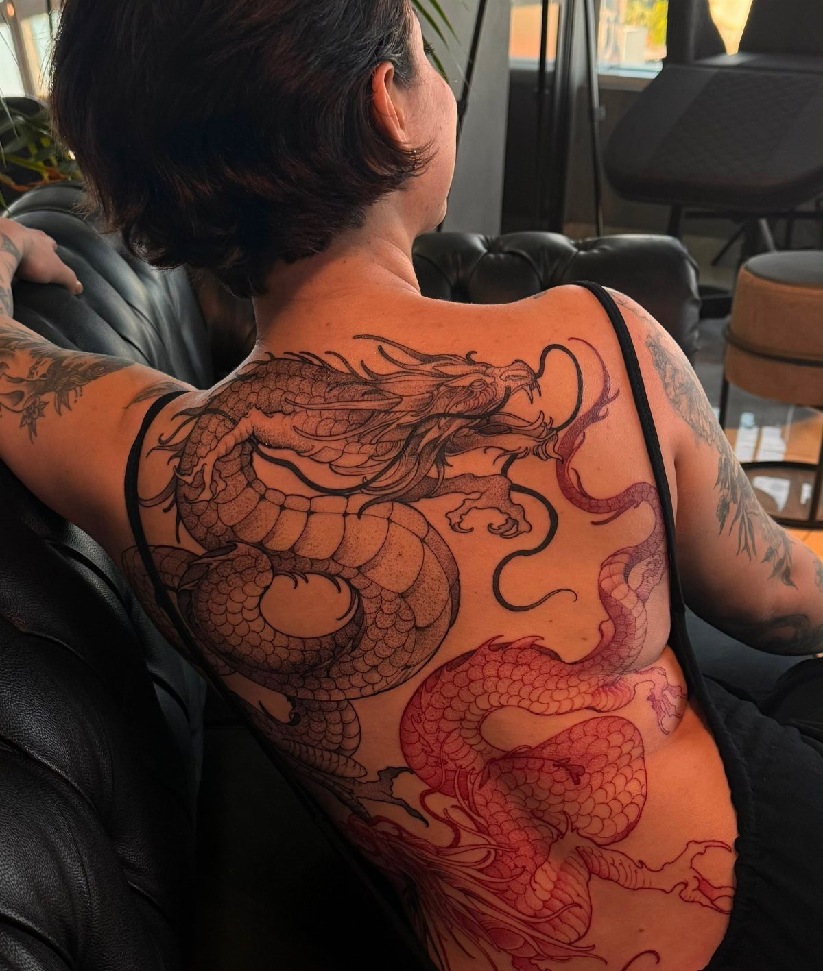 Two intertwined dragons, one black and one red, tattooed across a person's back.