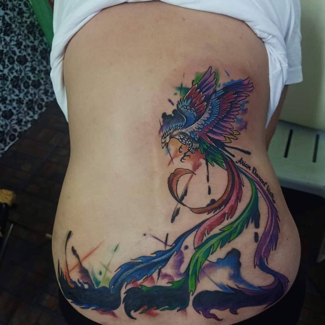 Colorful phoenix tattoo with vibrant feathers on a person's lower back.