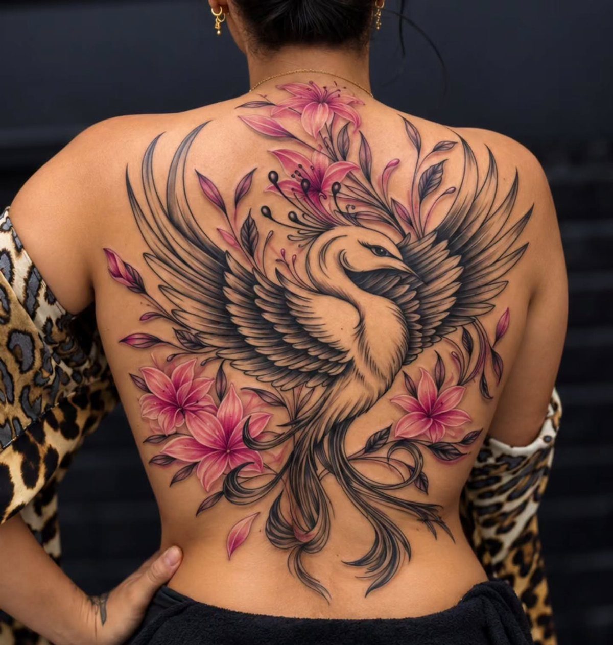 Phoenix tattoo on a back integrated with large pink lily flowers and leaves.