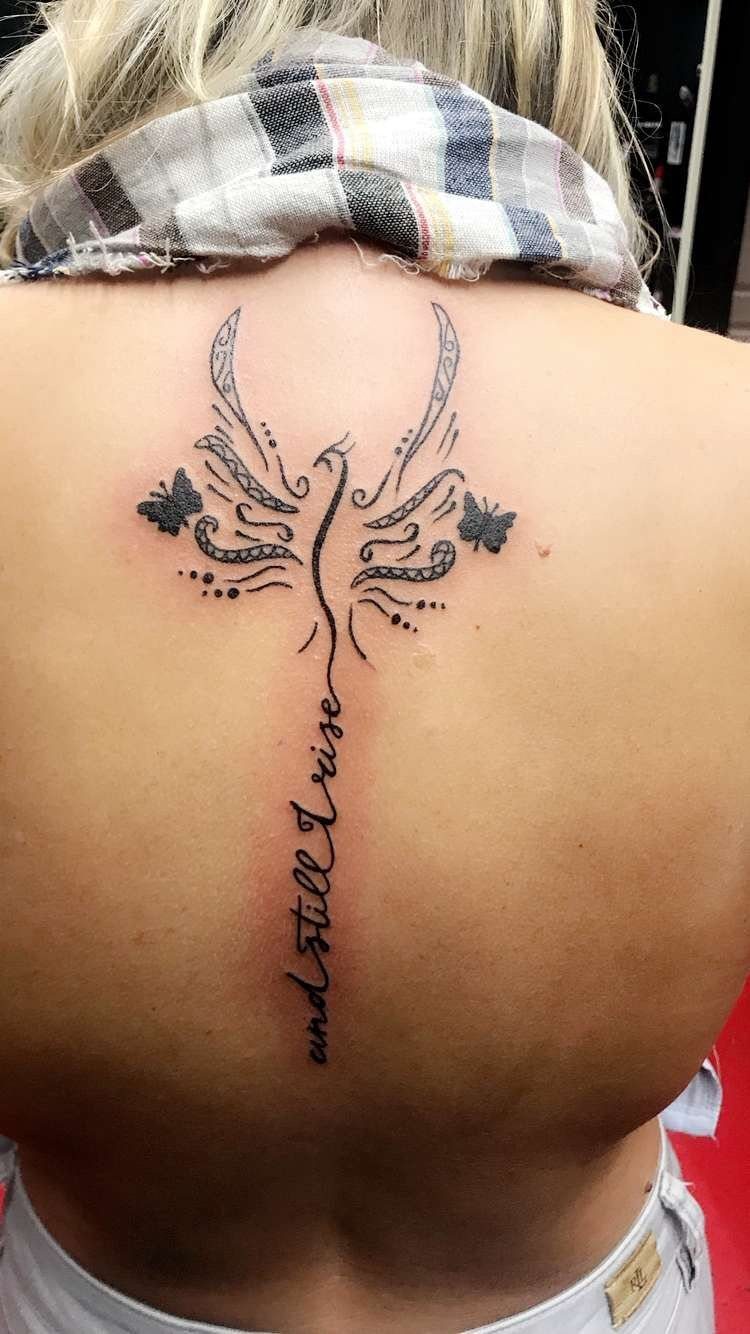 Phoenix tattoo on a back with butterflies and cursive script reading and still I rise