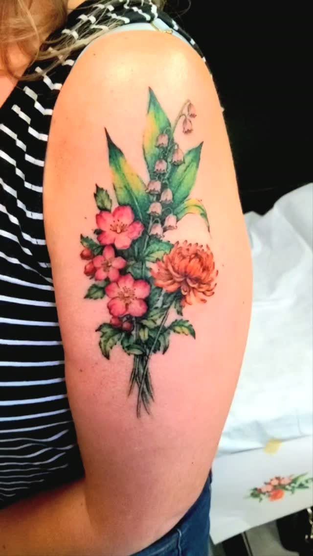 Colorful floral bouquet tattoo on an upper arm featuring pink and orange flowers.