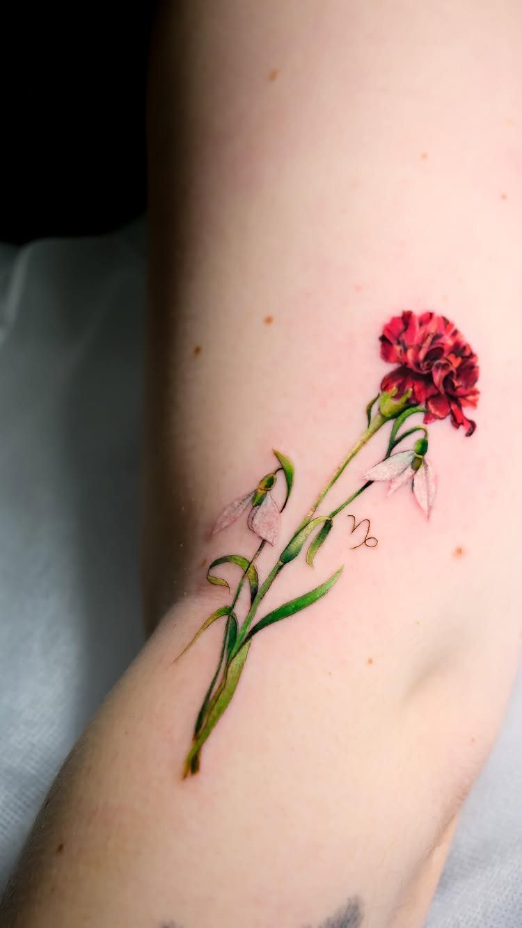 Red carnation and white snowdrop tattoo on a person's arm with zodiac symbol
