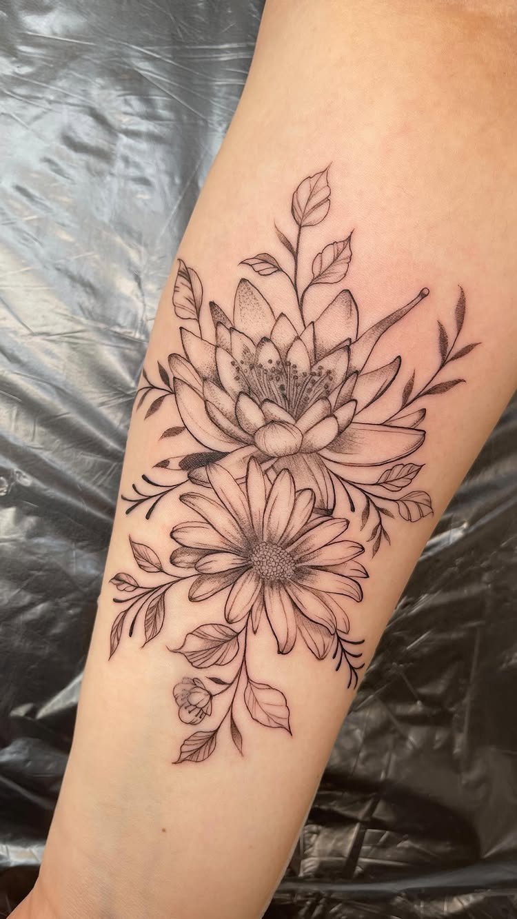 Daisy and lily flower tattoo in black ink on a person's forearm