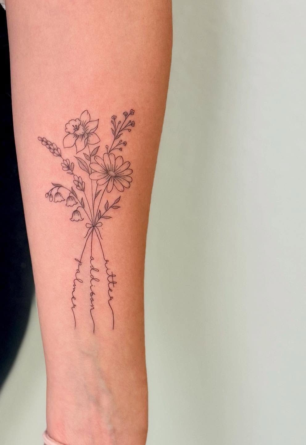 Bouquet of birth flower tattoo on forearm with names written below the stems