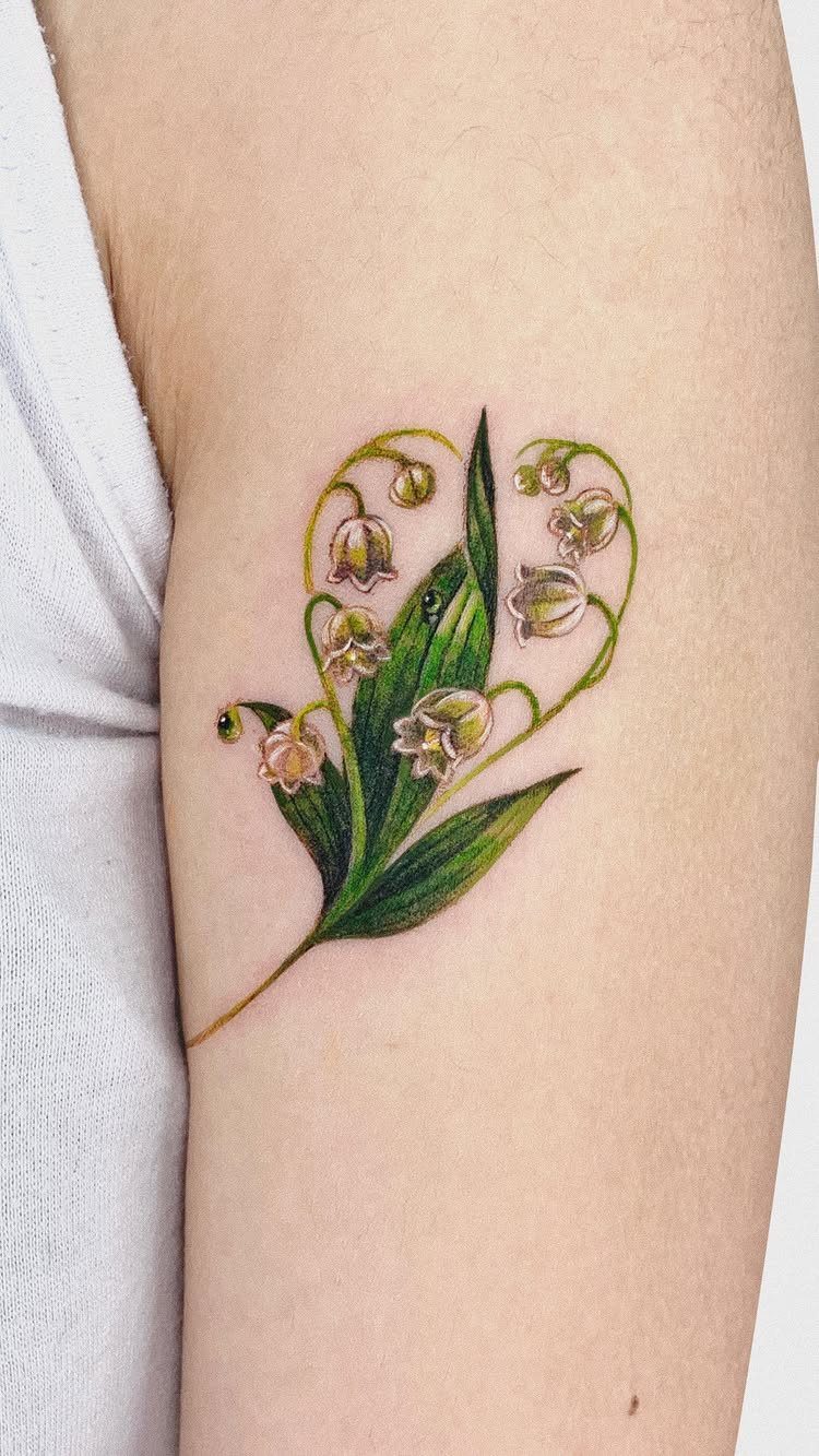 Lily of the valley tattoo with white bells and green leaves on an arm.