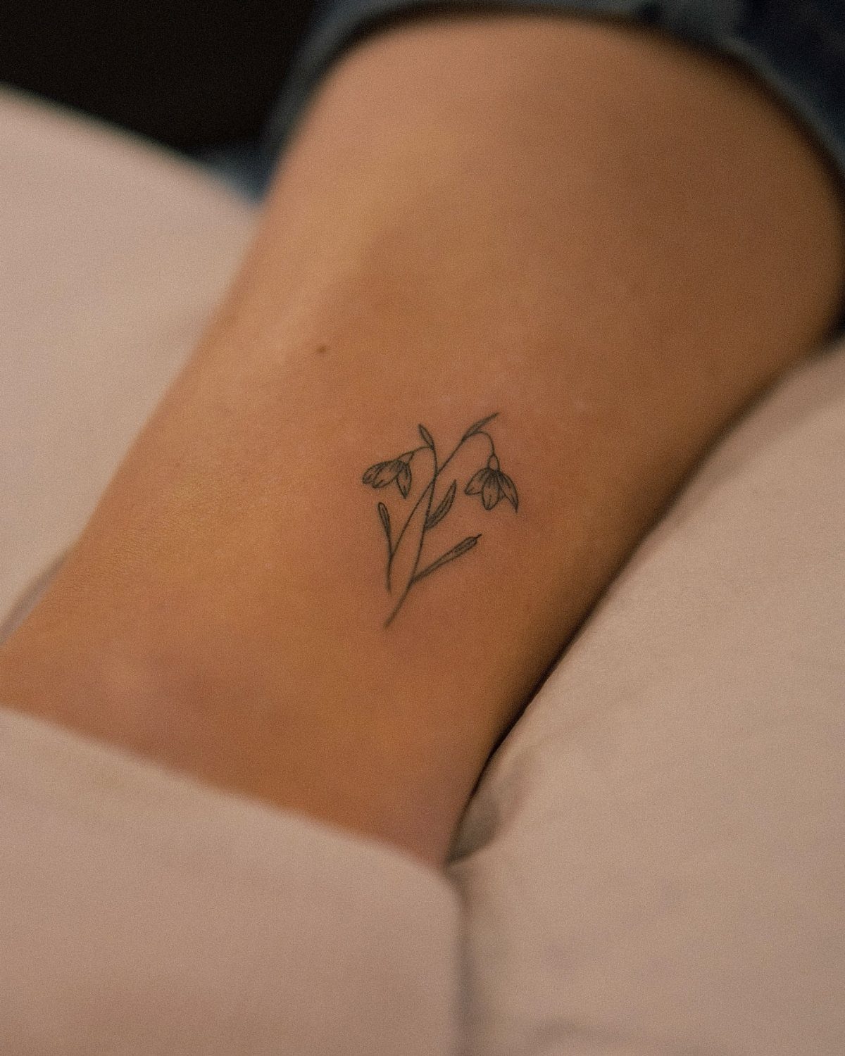 Small black ink snowdrop flower tattoo on a person's forearm
