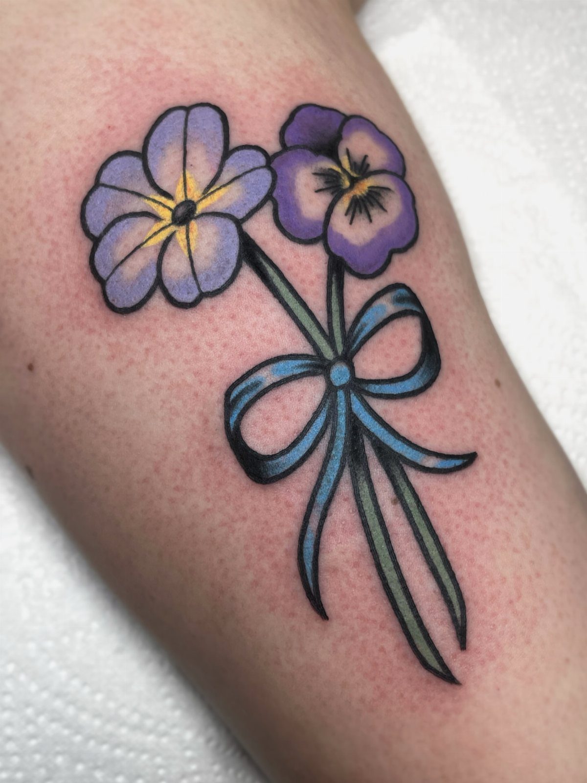 Two purple flower tattoos tied with a blue ribbon on human skin
