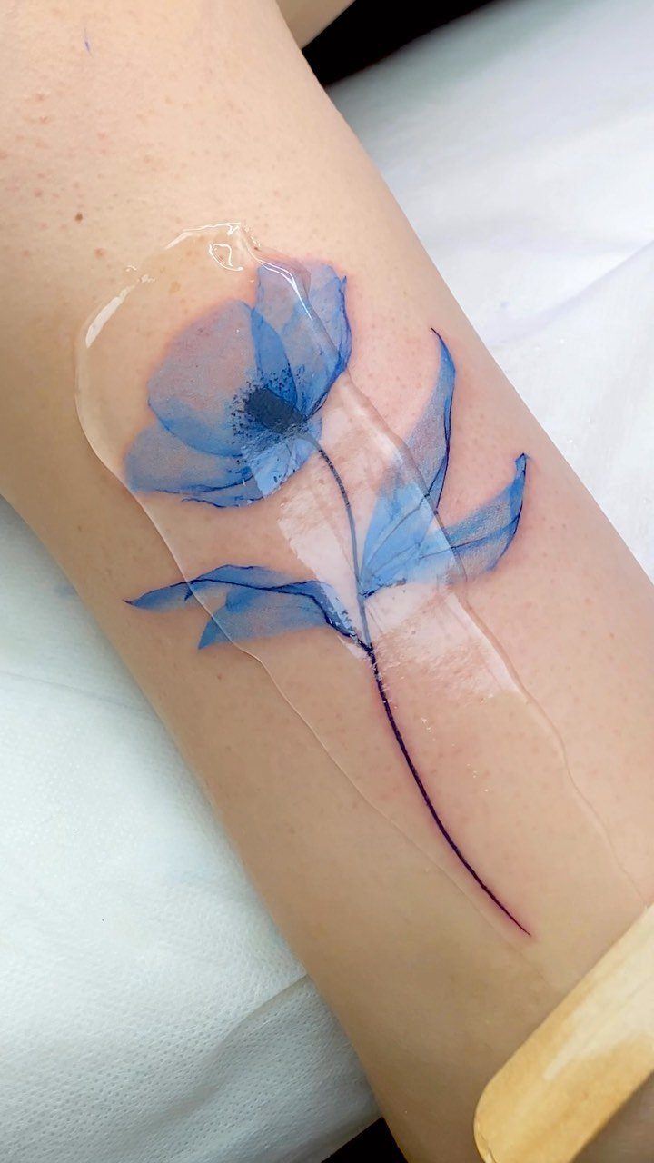 Blue poppy flower tattoo in watercolor style on a person's forearm