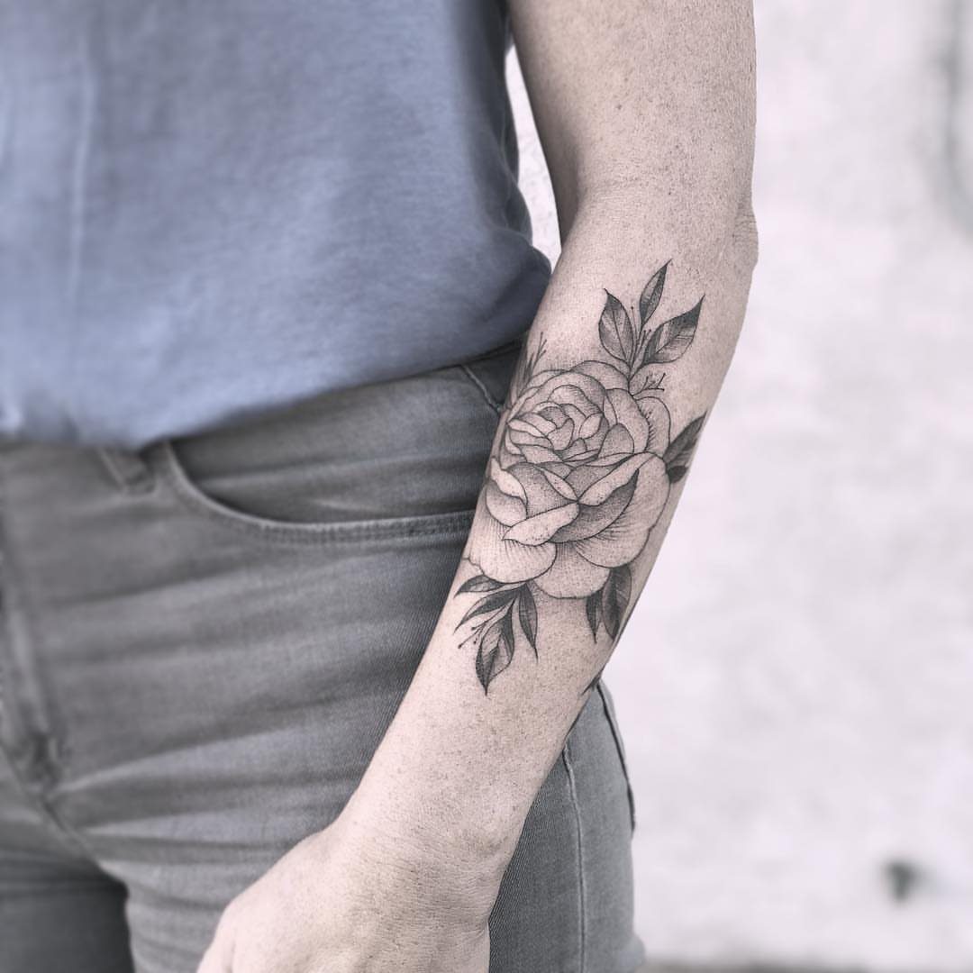 Black and gray rose tattoo with leaves on a person's inner forearm