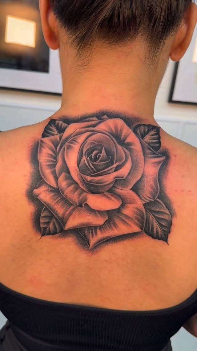 Detailed black and gray rose tattoo on the upper back and neck.