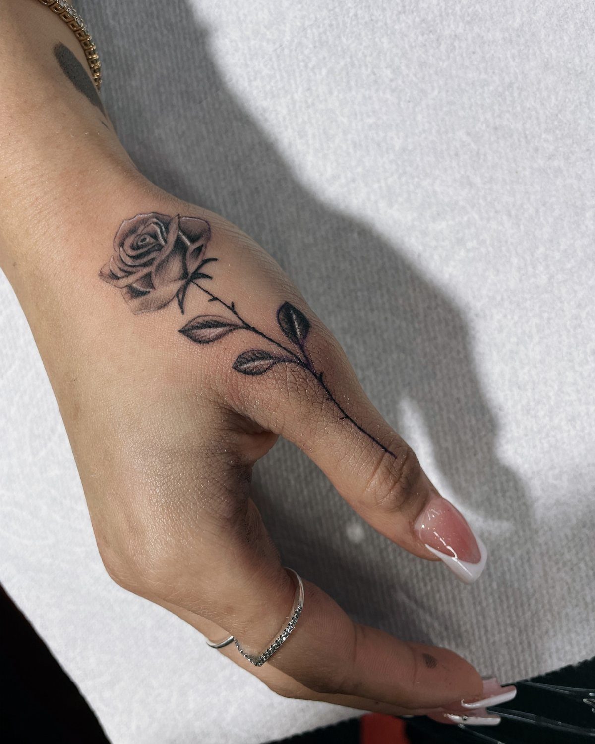 Black and gray rose tattoo on a hand extending down the index finger