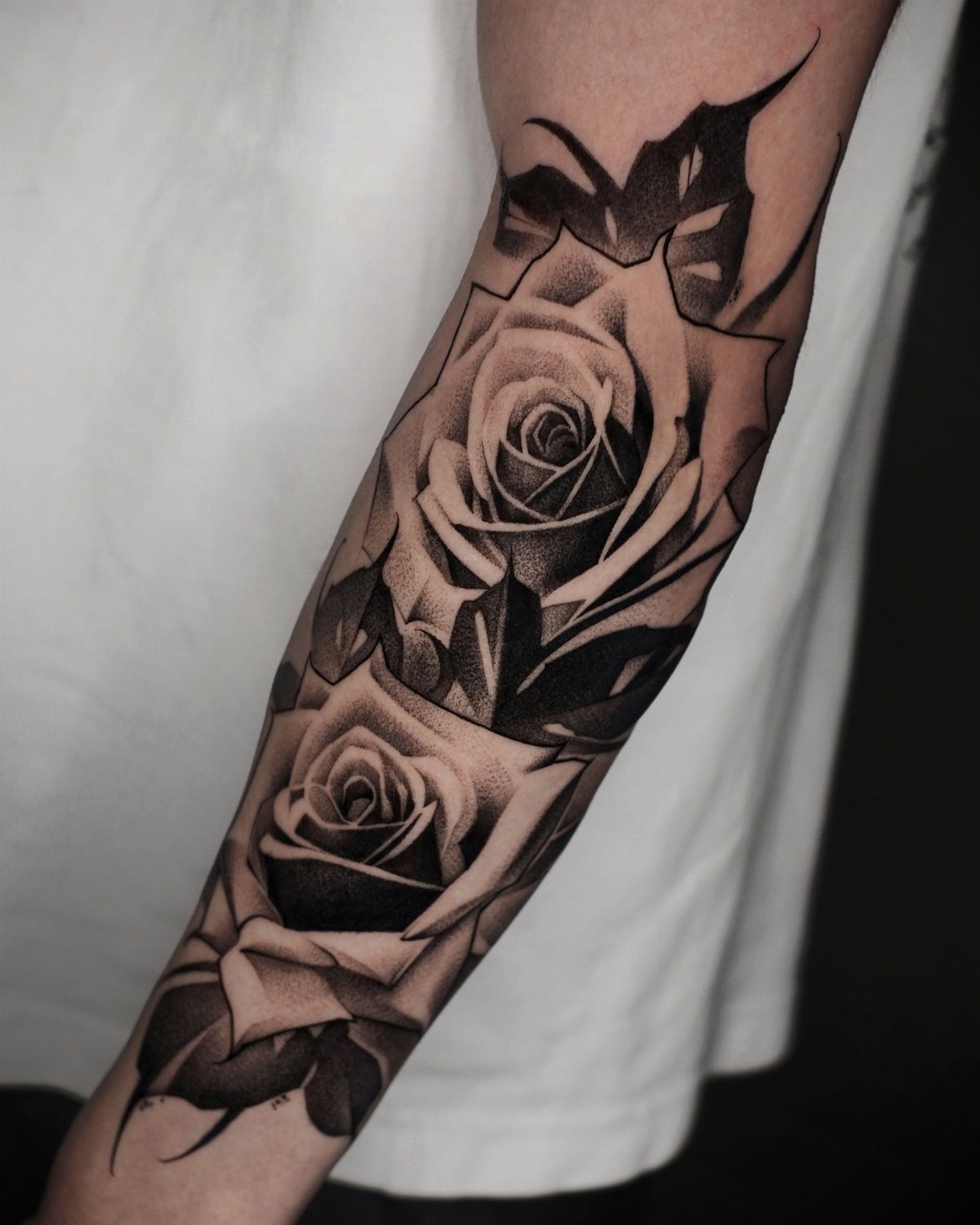 Two large black and gray rose tattoos with detailed shading on a forearm.