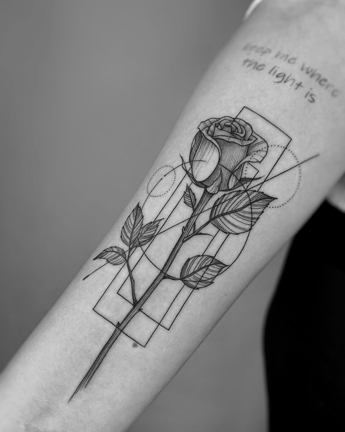 Geometric rose tattoo on a forearm with thin lines and circular elements.