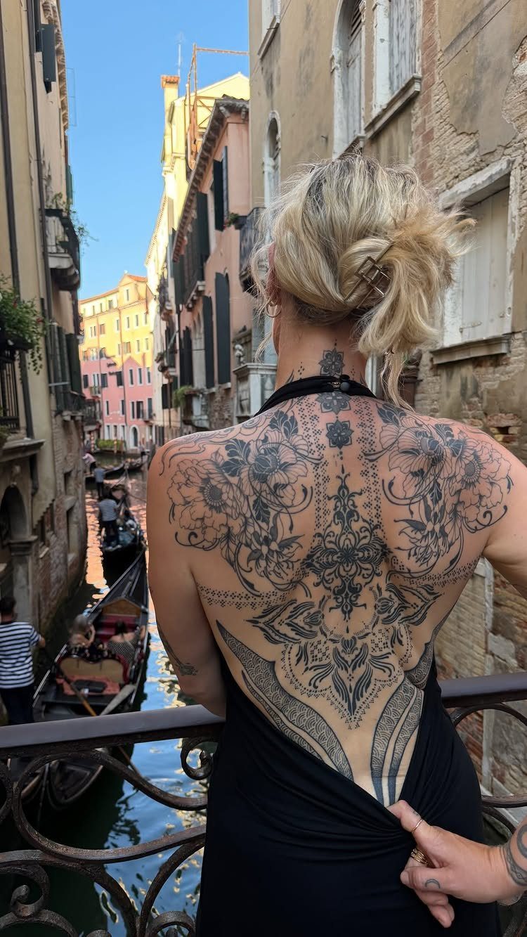 Woman's back featuring a large ornamental black ink tattoo with roses in Venice.