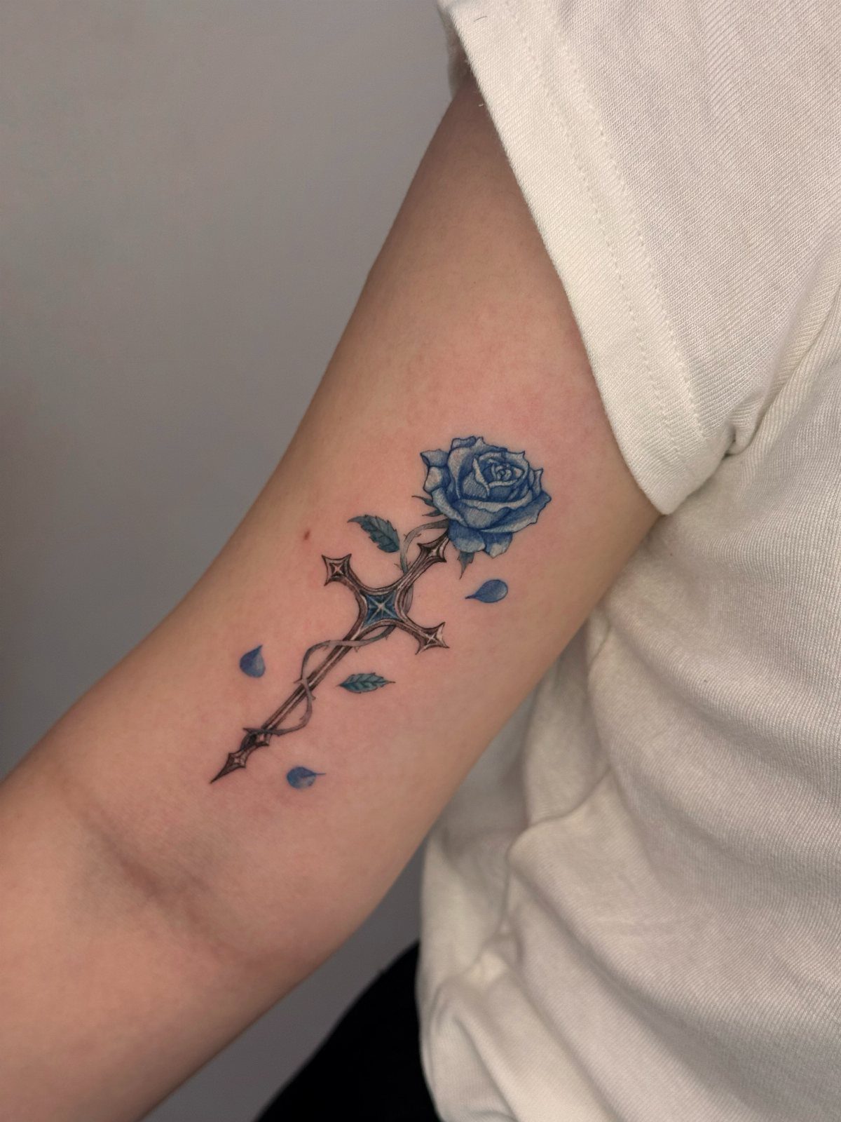 Blue rose and antique cross tattoo on a person's upper arm