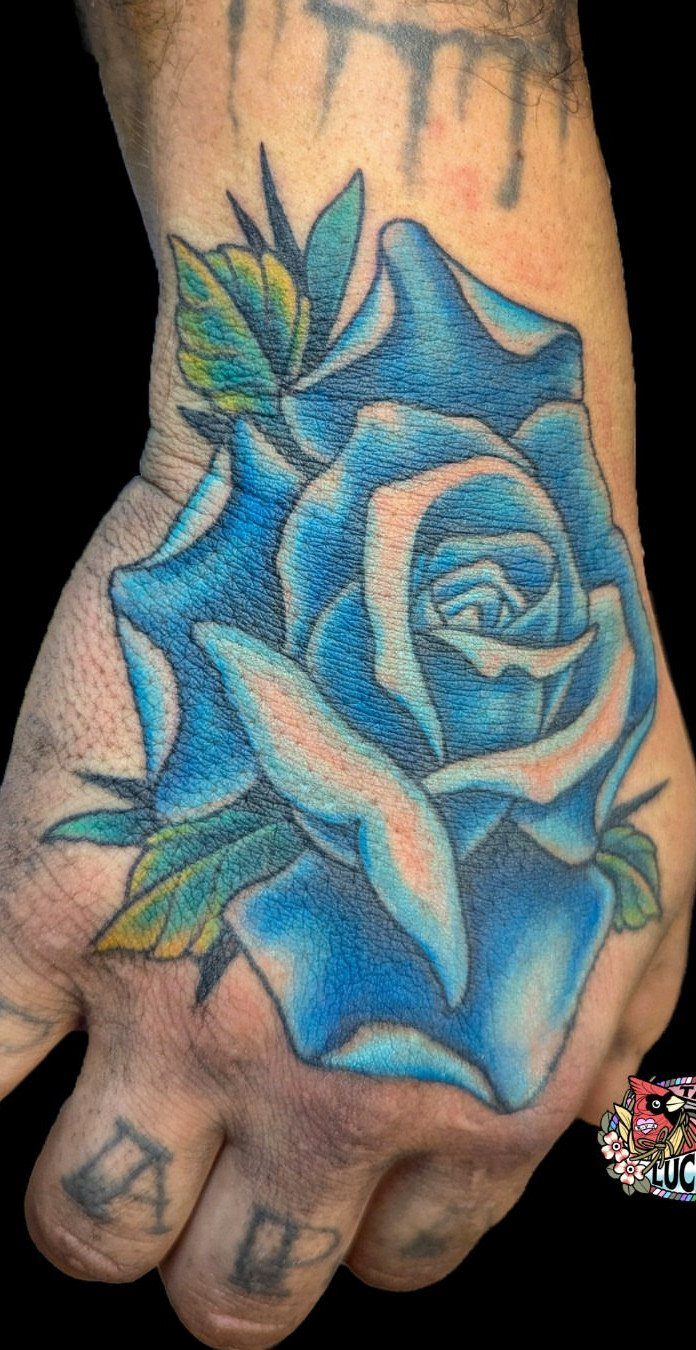 Vivid blue rose tattoo with green leaves on the back of a hand.
