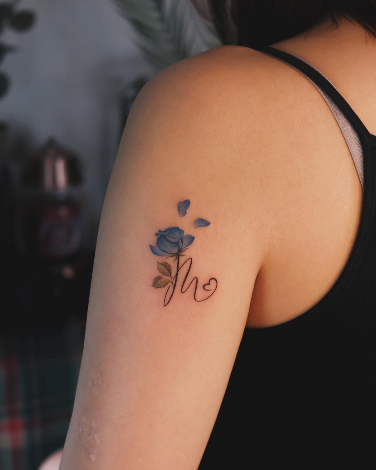 Blue rose tattoo with a letter M on a person's upper arm