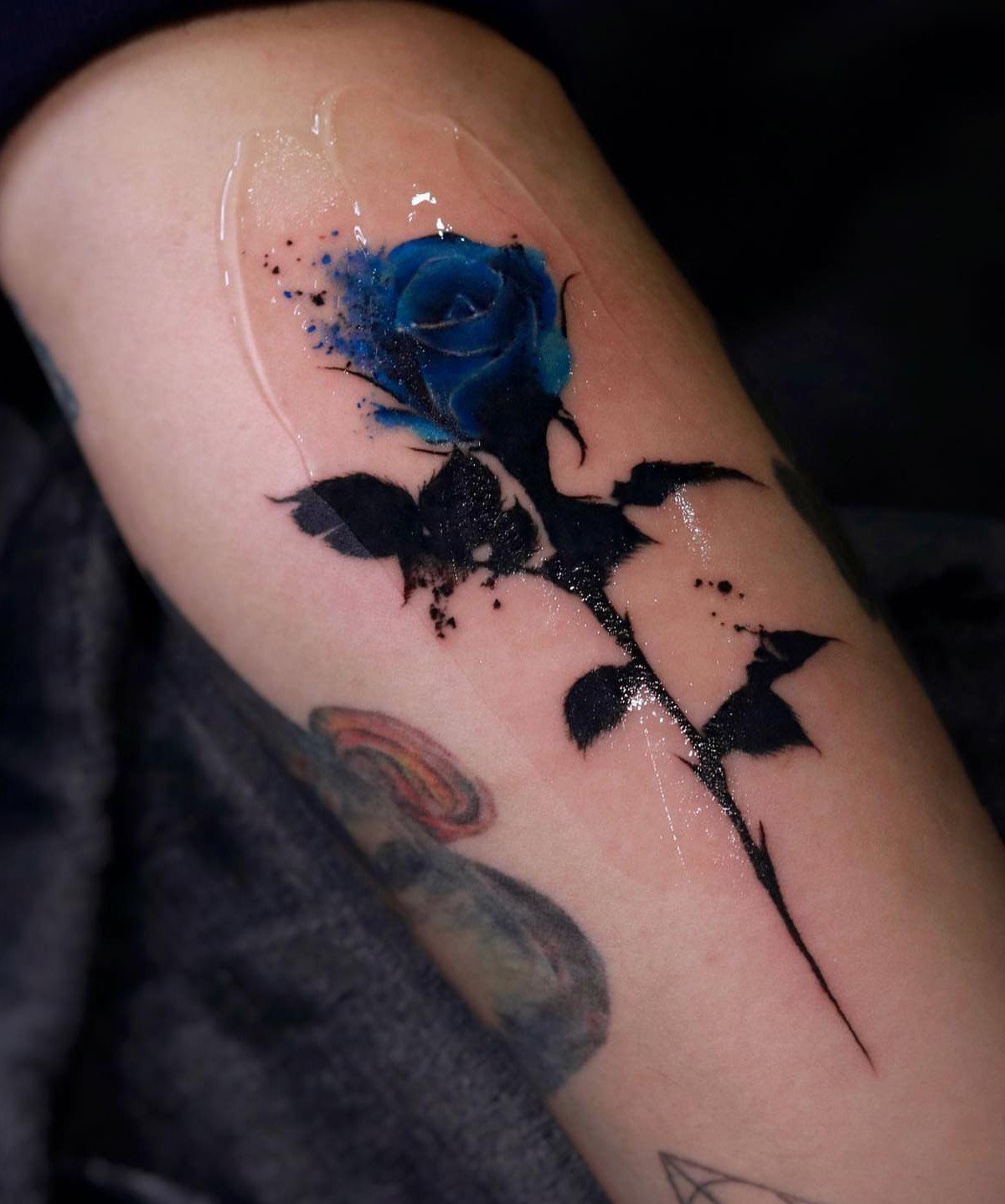 Blue rose tattoo with black leaves on an upper arm under protective film