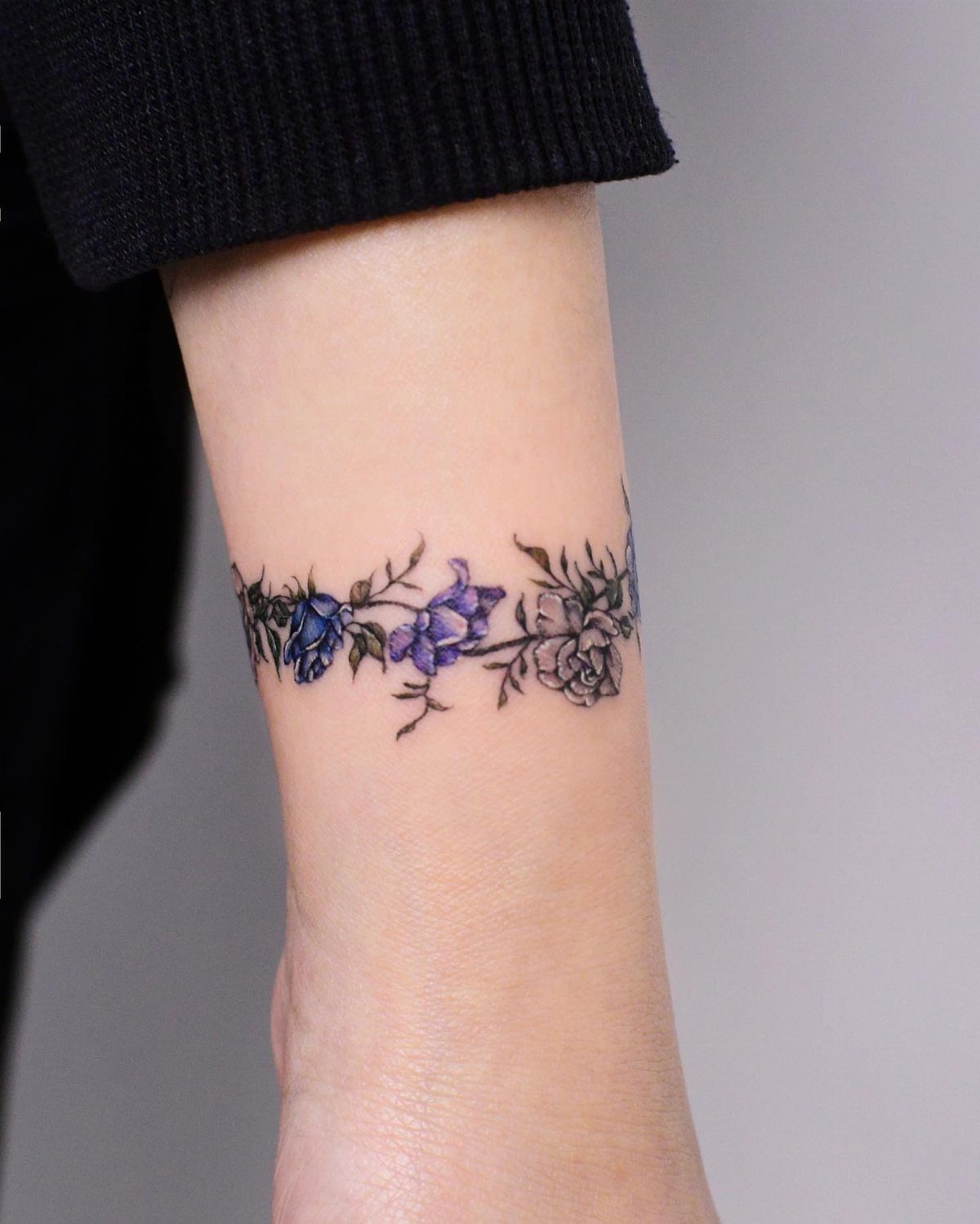 Blue and purple rose tattoo wrapping around a person's wrist as a floral band.