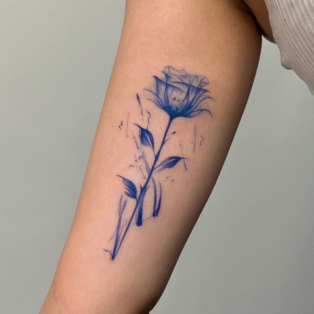 Blue rose tattoo with stem and leaves on a person's forearm