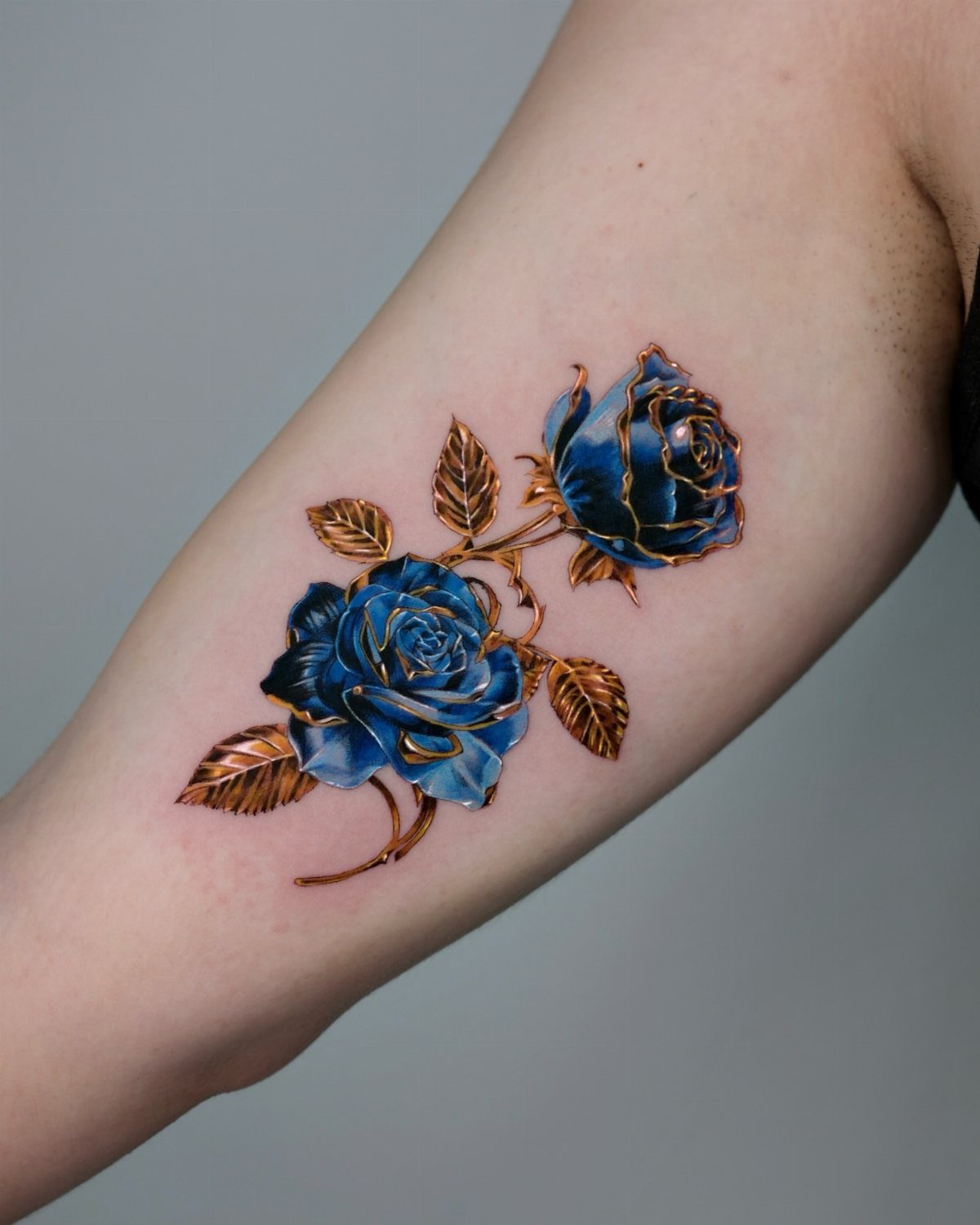 Two realistic blue roses with copper leaves tattooed on a person's forearm