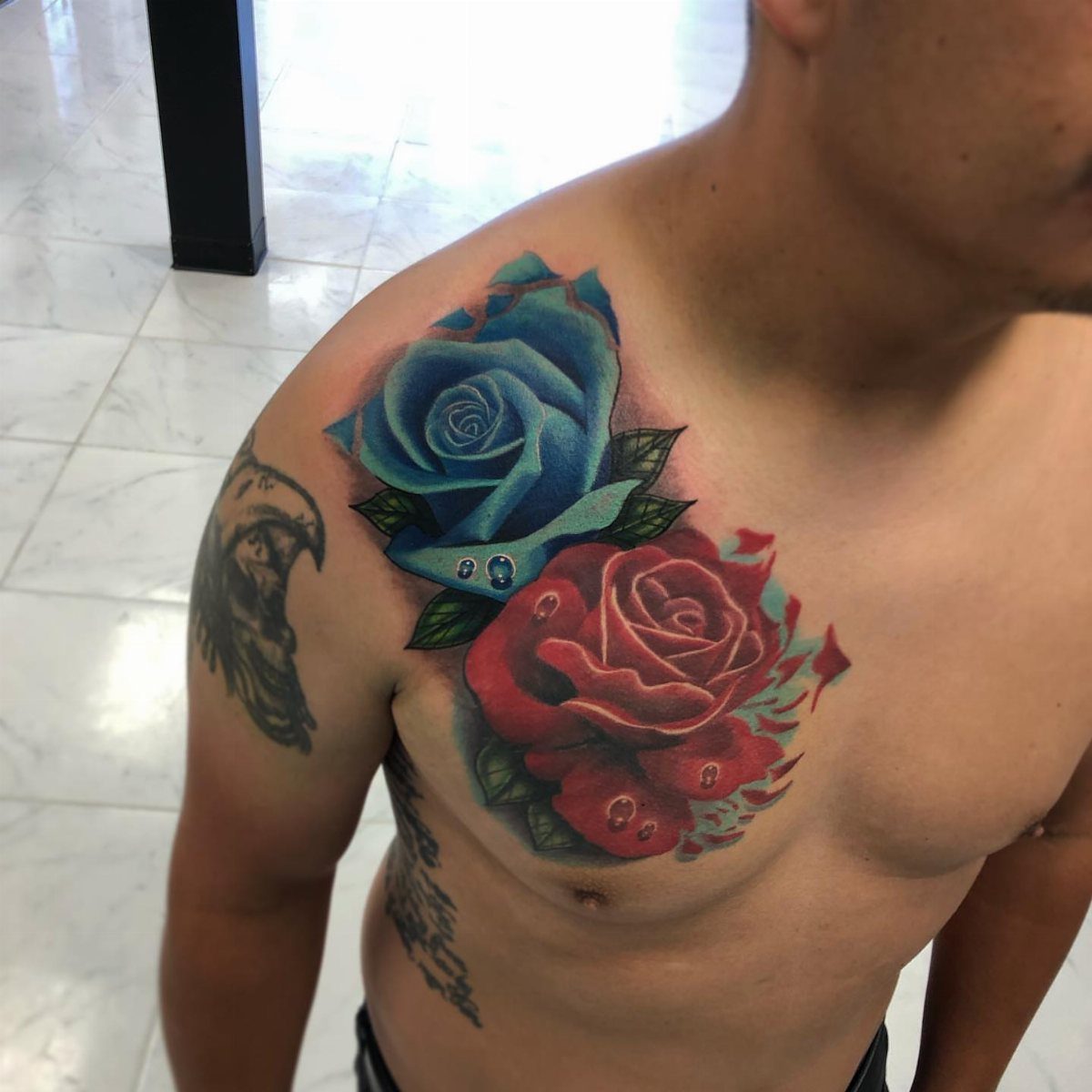 Red and blue rose tattoos on a man's chest and shoulder area.