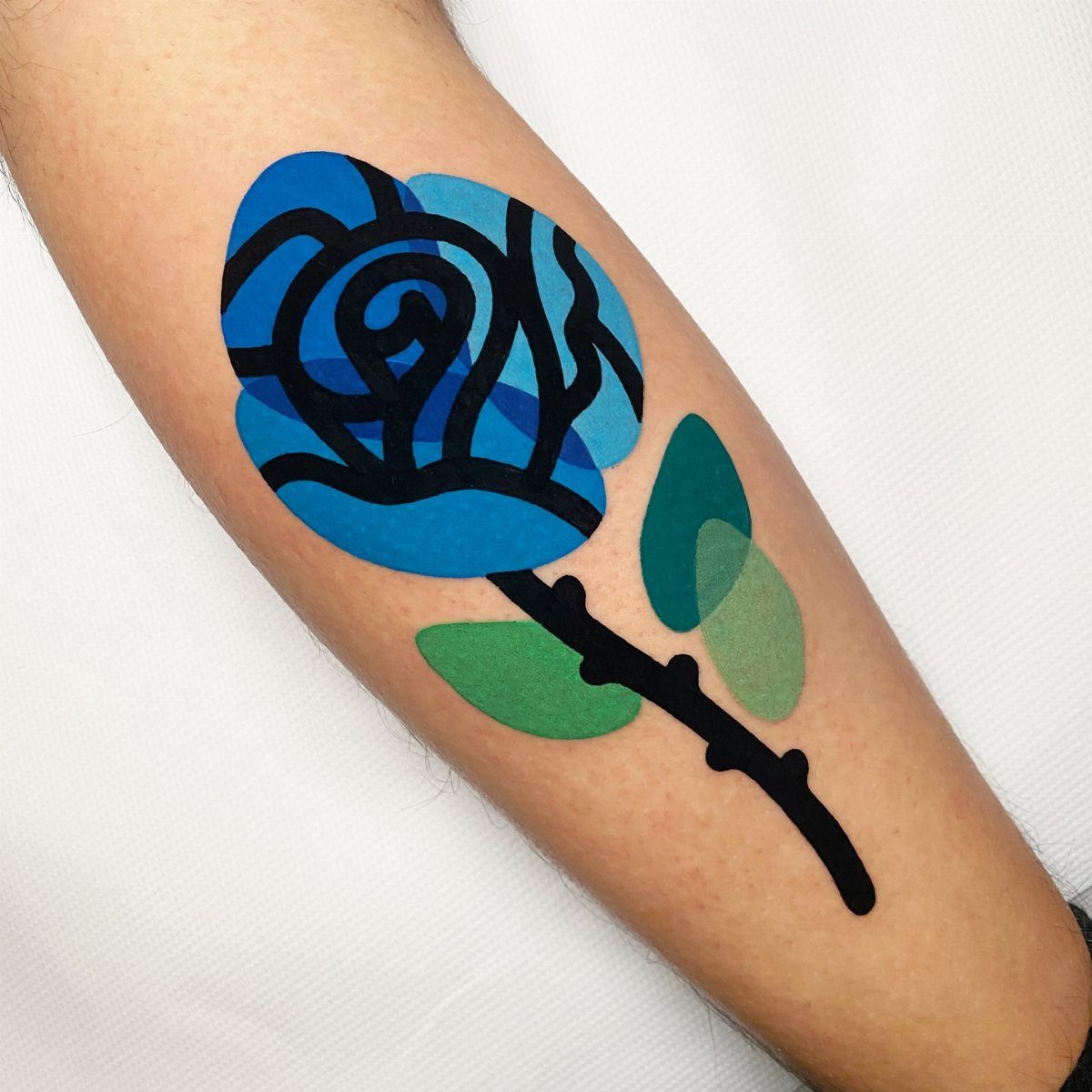 Stylized blue rose tattoo with green leaves on a person's forearm