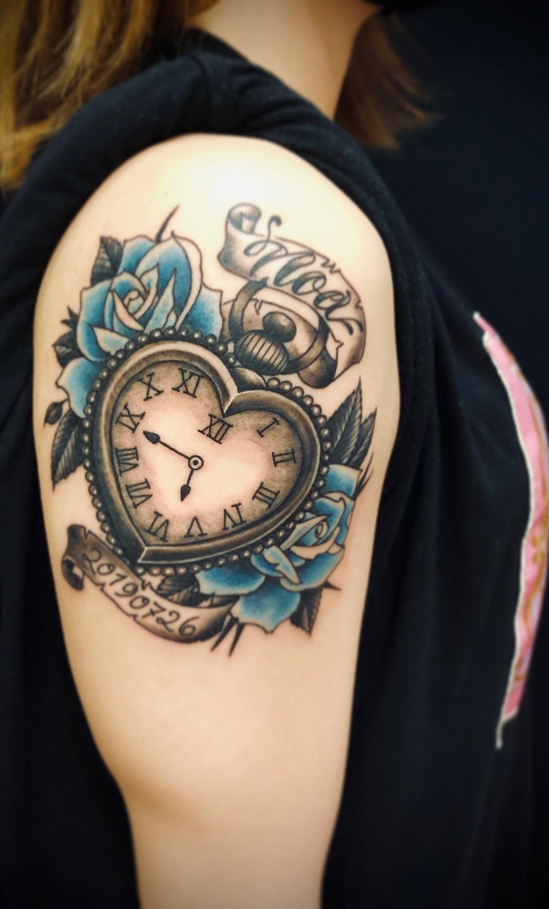 Heart-shaped pocket watch tattoo surrounded by blue roses on an upper arm