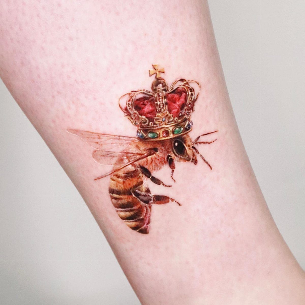 Bumble bee tattoo wearing a royal gold crown on a person's forearm