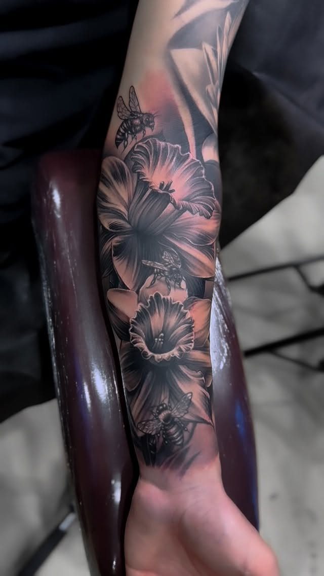 Bumble bee tattoo with large flowers on a person's forearm in black and grey.