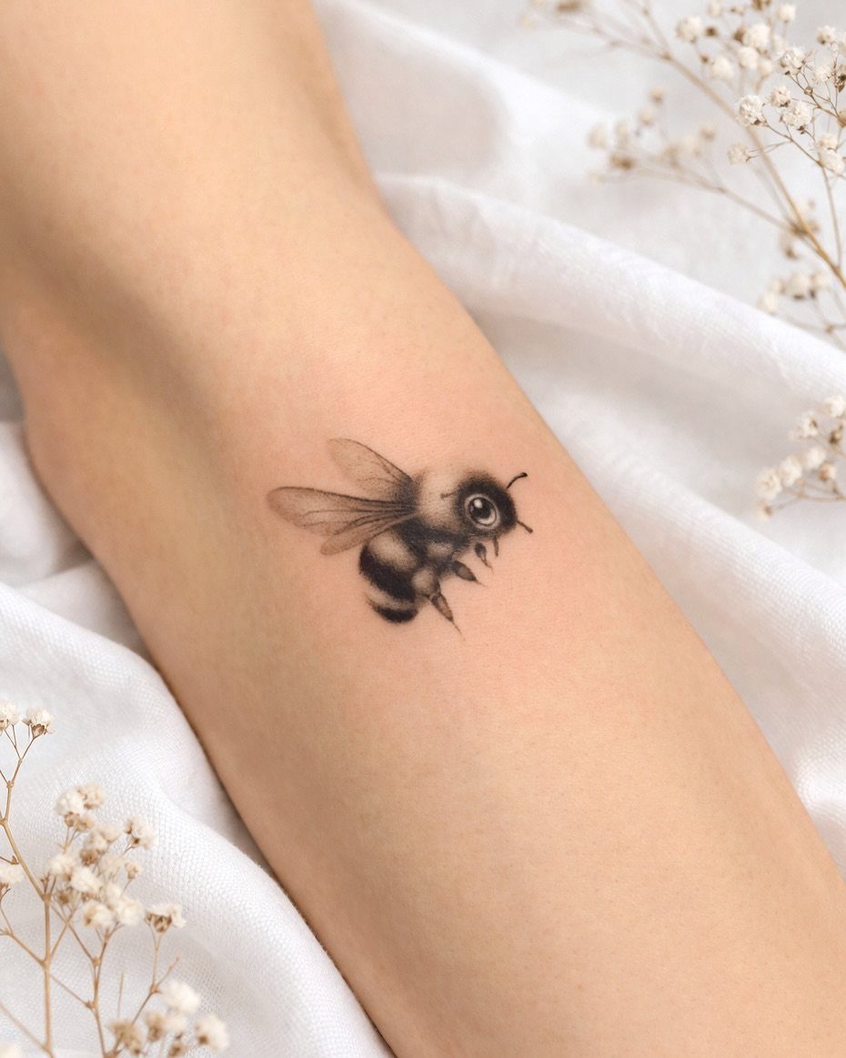 Bumble bee tattoo on a forearm with white fabric and dried flowers background