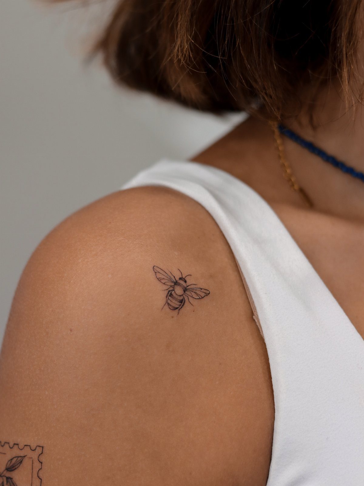 Bumble bee outline tattoo on a person's shoulder wearing a white top.