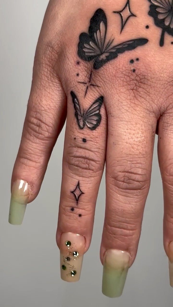 Black butterfly and star tattoos on a hand with long manicured nails