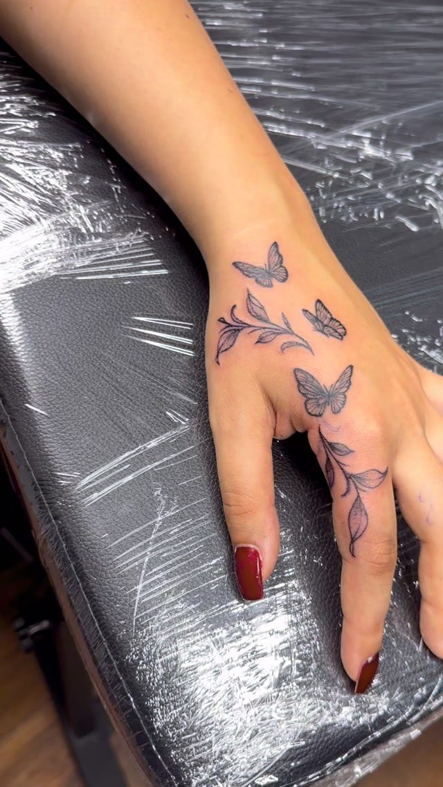 Black butterfly and flower tattoos on the back of a person's hand.