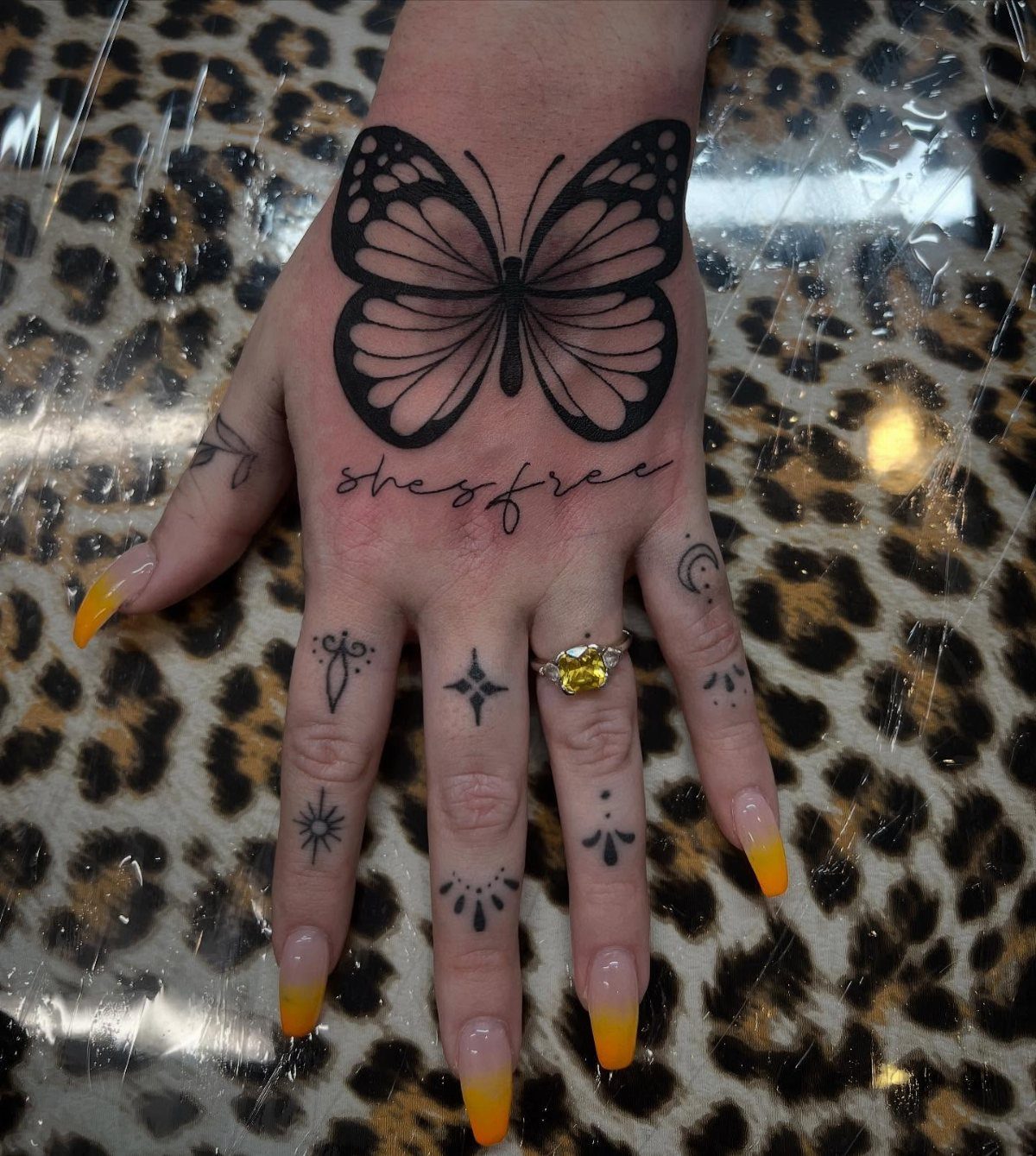 Butterfly tattoo on the back of a hand with yellow manicured nails