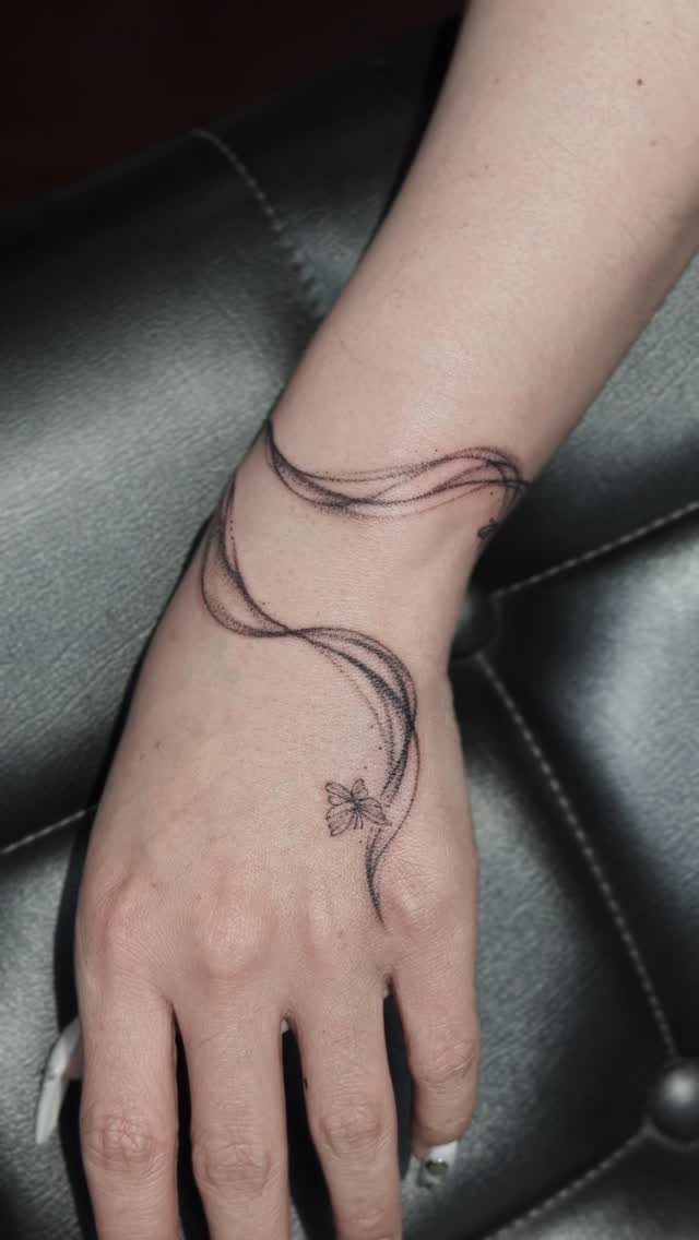 Hand and wrist with a black ink tattoo of flowing curves and a butterfly.