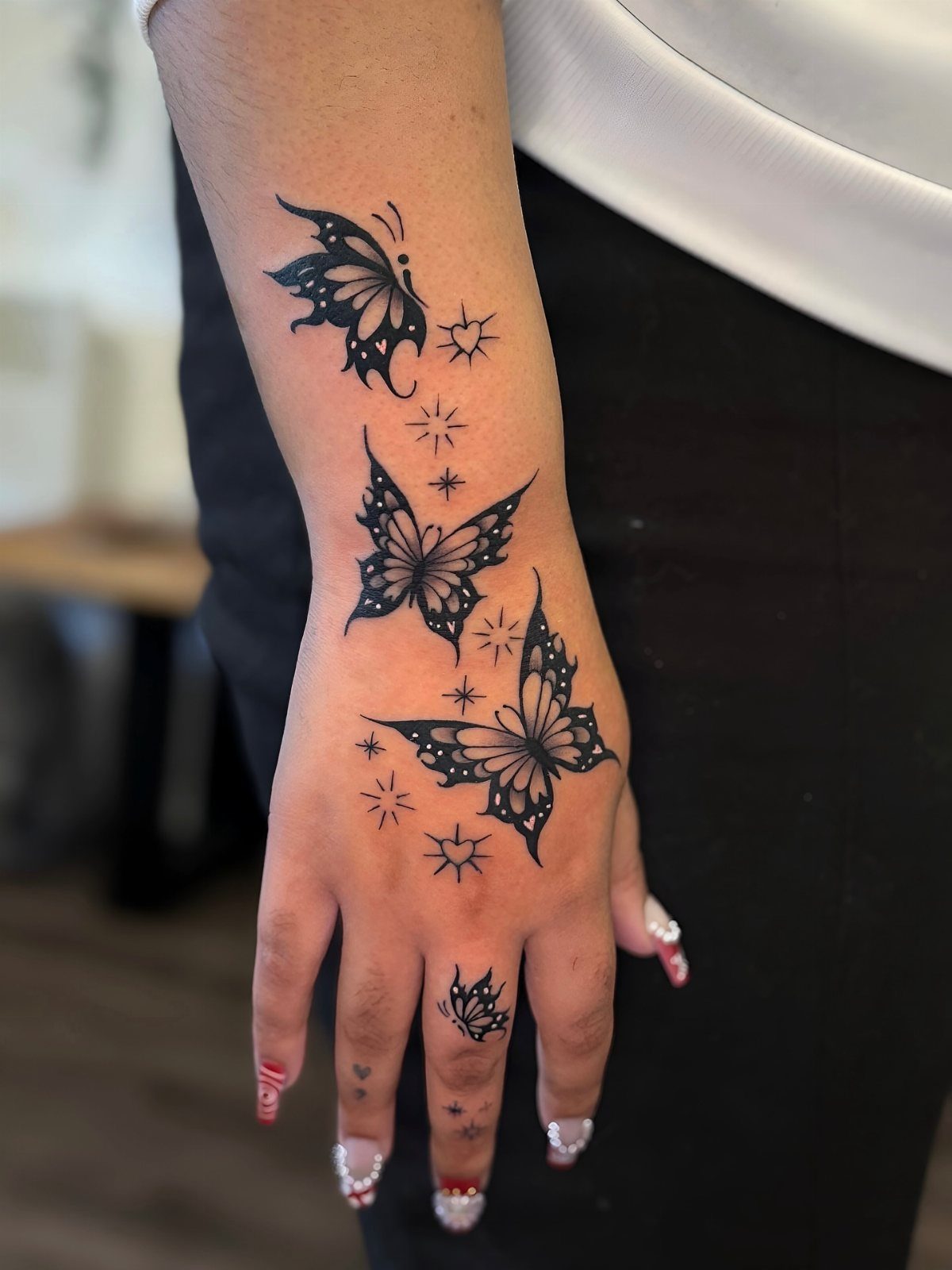 Hand and wrist with black ink butterfly tattoos and small decorative stars.