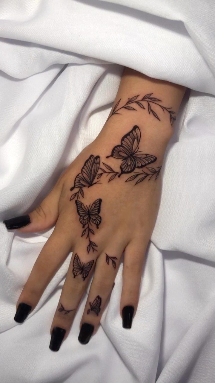 Hand and wrist with black butterfly and vine tattoos against white fabric