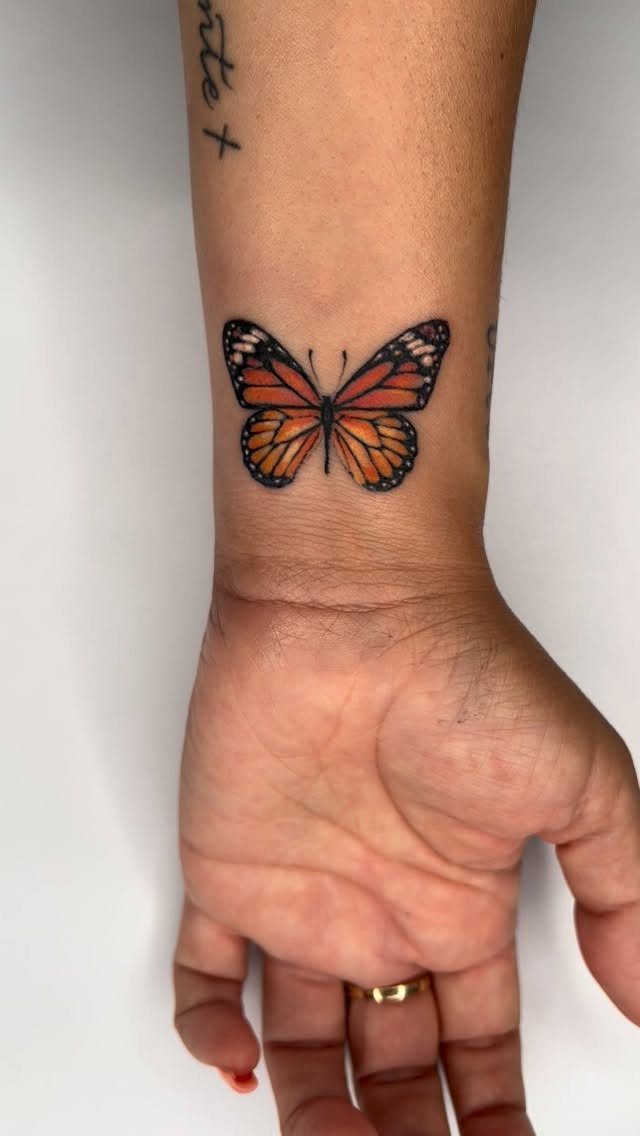 Monarch butterfly tattoo on a person's wrist with a gold ring on finger