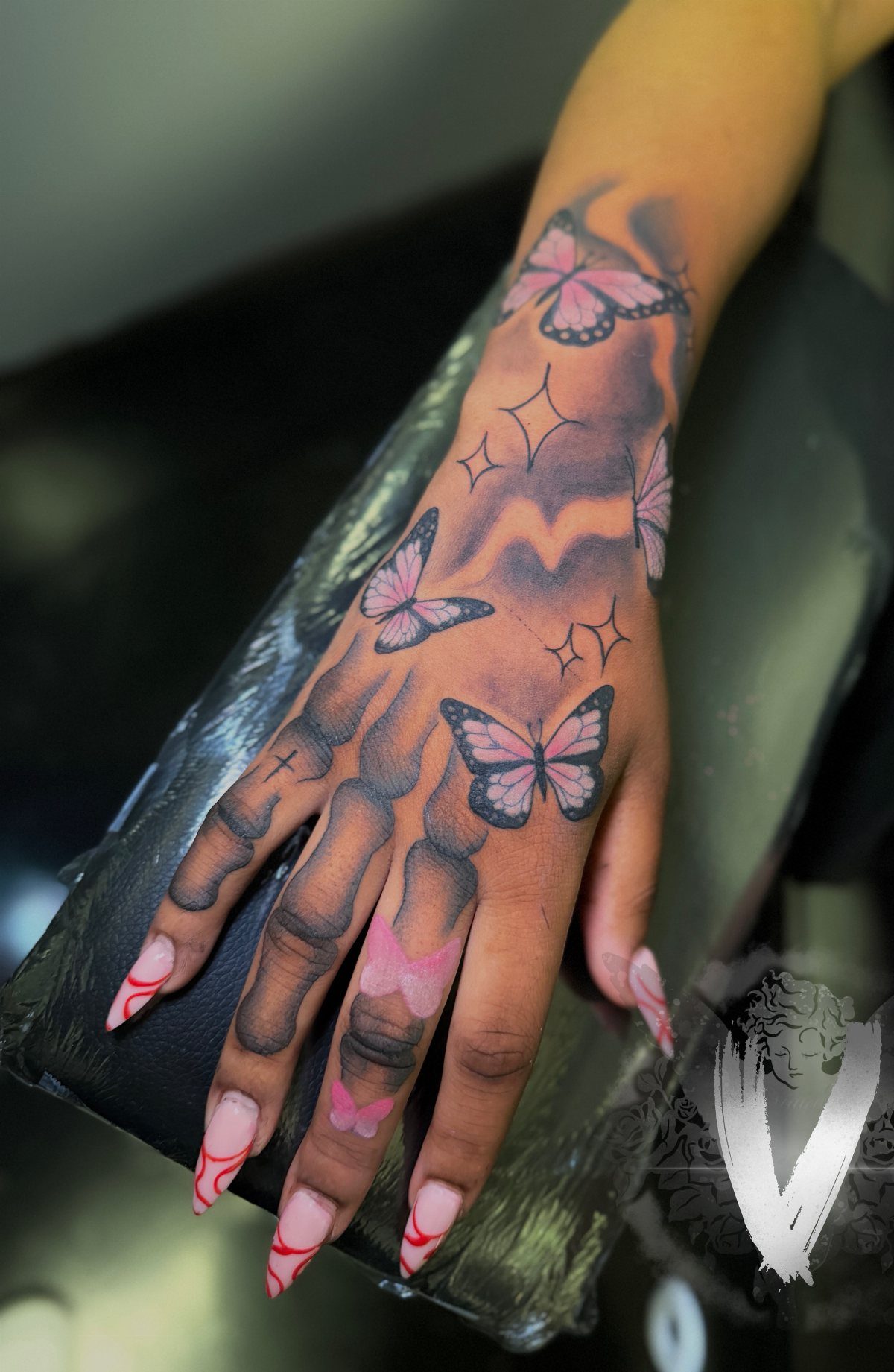 Hand and wrist with pink and black butterfly tattoos and long decorated nails.