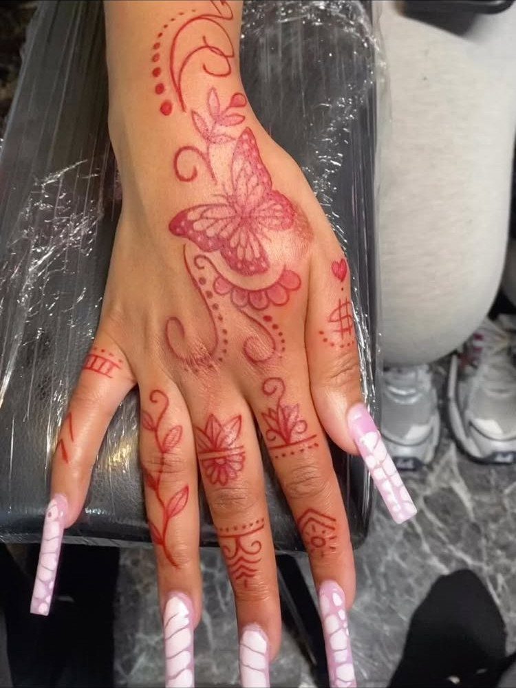 Red butterfly tattoo on the back of a hand with floral finger accents