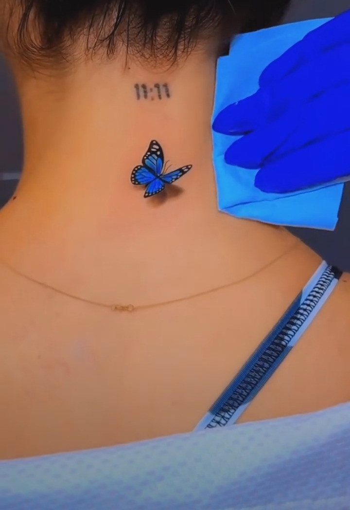 Blue butterfly tattoo on the back of a neck with 11:11 numbers above.