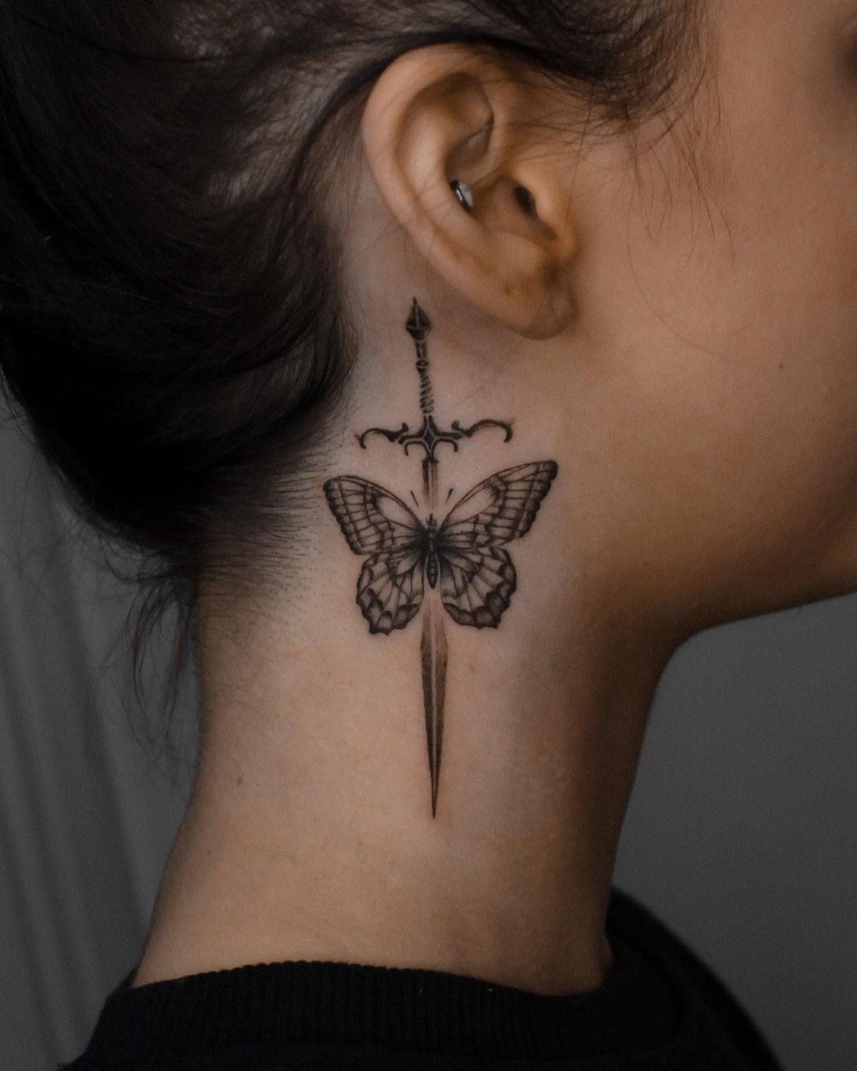 Butterfly with dagger tattoo on the side of a person's neck