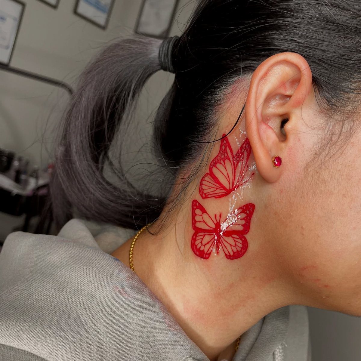 Two red fine-lined butterfly outline tattoos on the side of a person's neck.